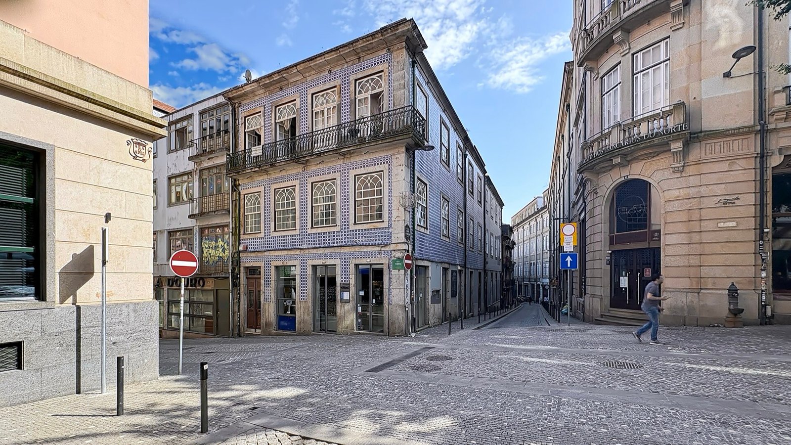 Esquina com azulejo azul e branco numa rua portuguesa, com uma pessoa a caminhar sozinha